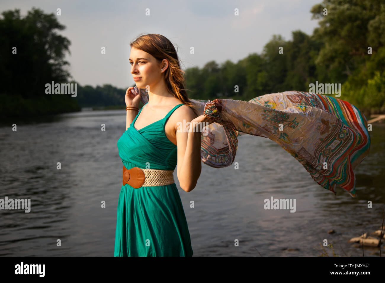 Junge Frau mit einem blaugrün Kleid steht an einem Fluss / See holding im Wind flatternden Teal trendigen Schal.   Sie ist entspannt und ruhig während Gefühl t Stockfoto