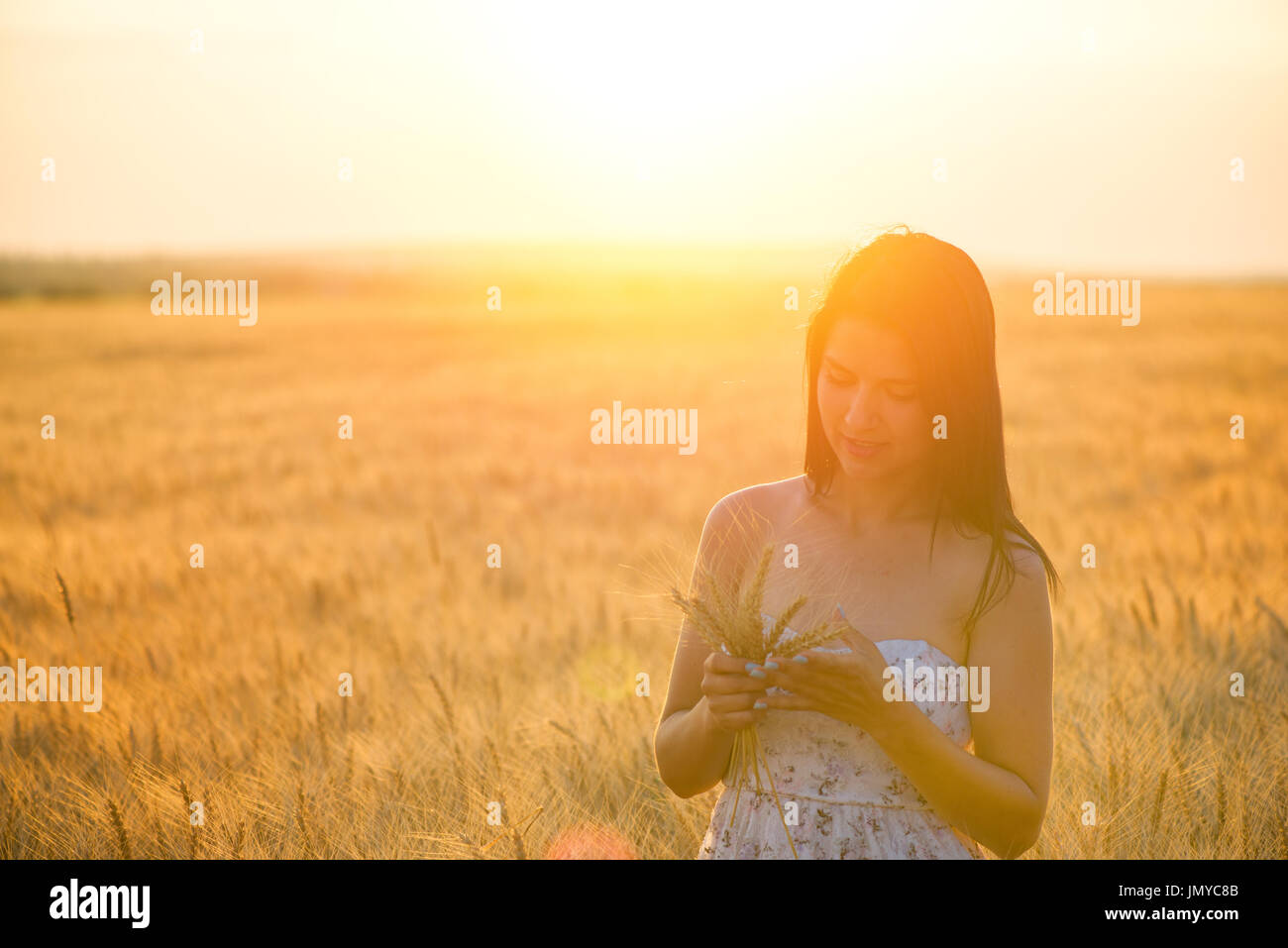 schöne Frau mit einem Weizen-Blumenarrangement im Weizenfeld bei Sonnenuntergang Stockfoto