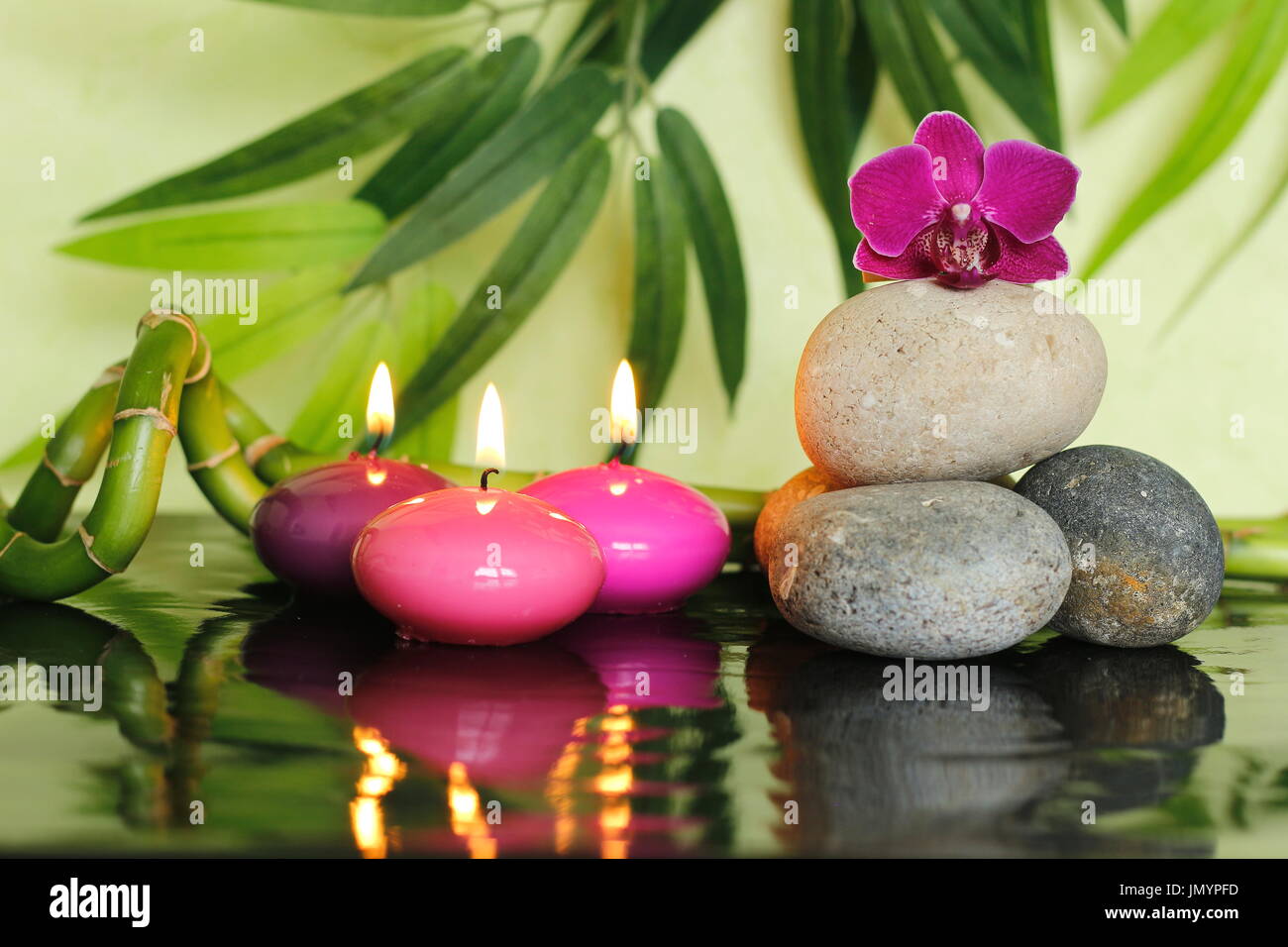 Kieselsteine in Zen Lebensstil auf der rechten Seite angeordnet, mit einer Orchidee auf die Spitze und rosa Kerzen angezündet Stockfoto