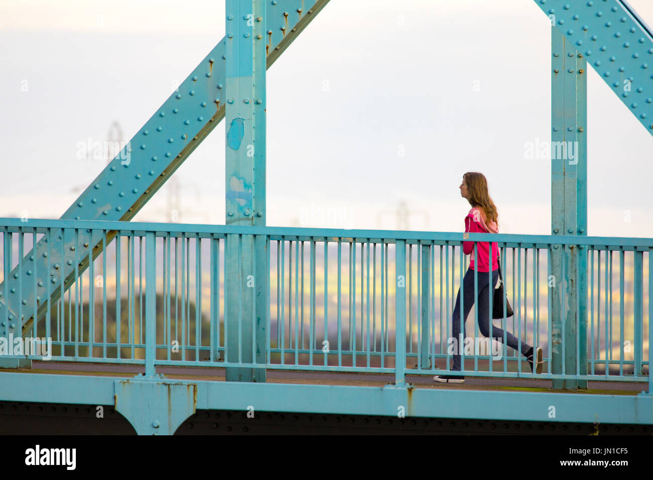 Eine Frau zu Fuß am frühen Morgen über die blauen Jubiläums-Brücke bei Queensferrry, die überquert den Fluss Dee und Mündung in Flinthsire, Wales, UK Stockfoto