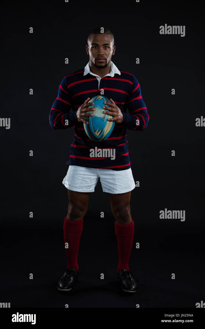 Porträt des Sportlers mit Rugby-Ball stehend auf schwarzem Hintergrund Stockfoto