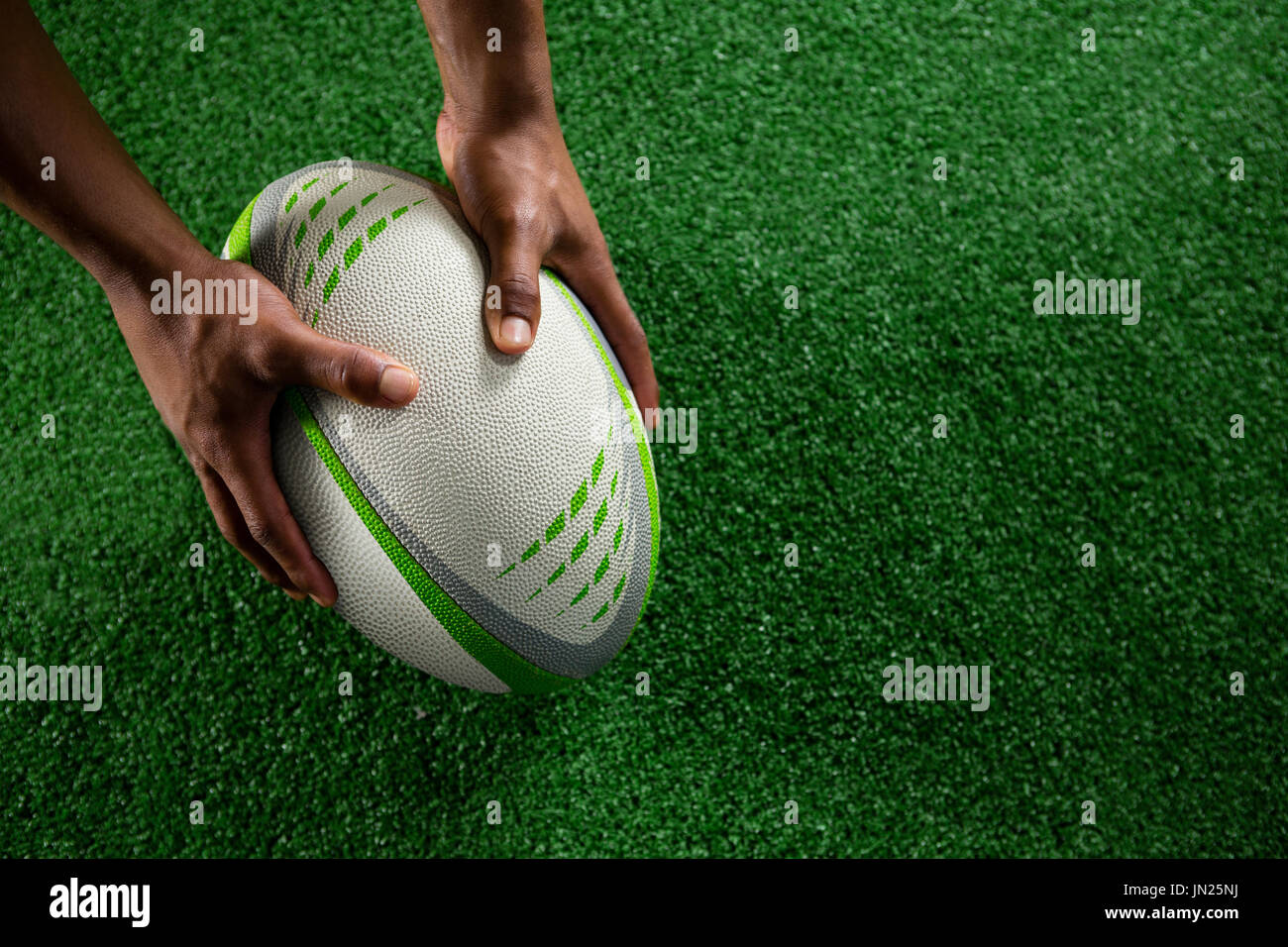 Erhöhte Ansicht von Händen mit Rugby-Ball auf Feld Stockfoto