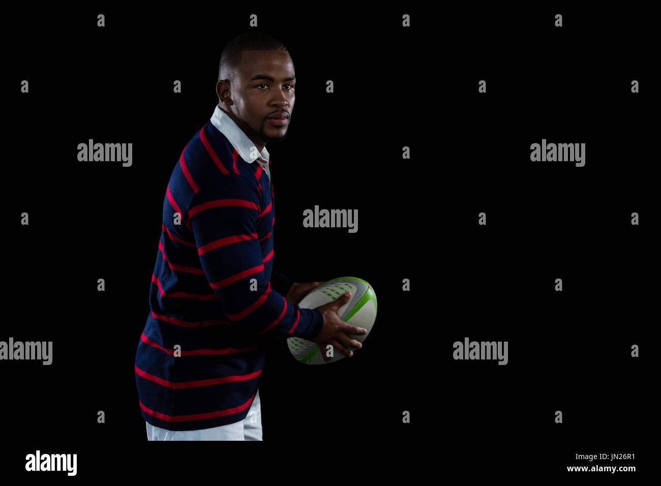 Seitenansicht des männlichen Athleten mit Rugby-Ball stehend auf schwarzem Hintergrund Stockfoto