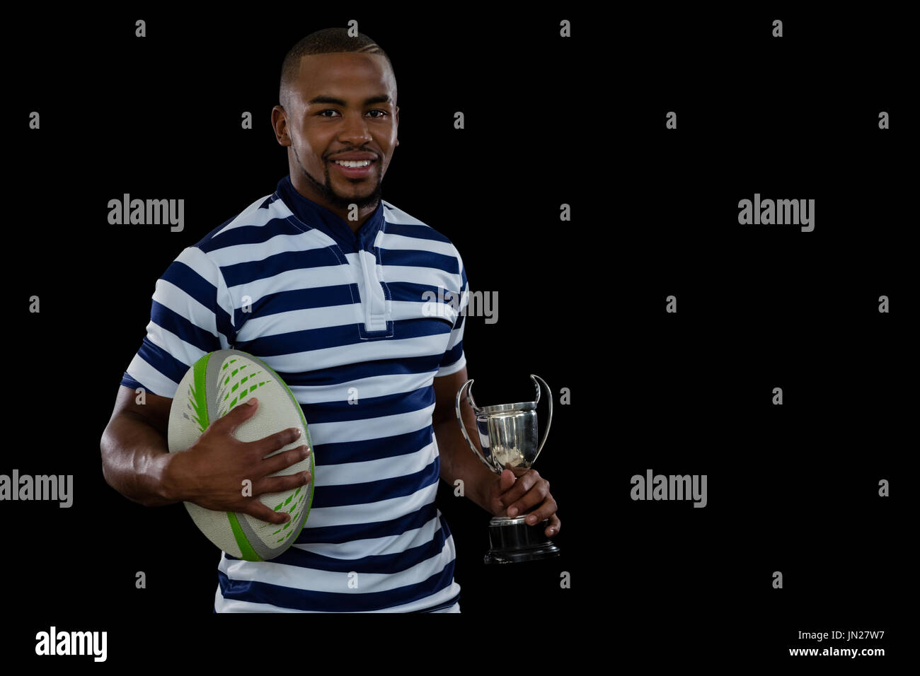 Portrait männlicher Athlet mit Rugby-Ball und Trophäe vor schwarzem Hintergrund Stockfoto