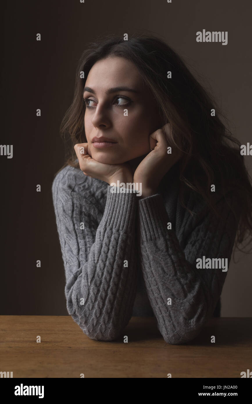 Nachdenkliche Frau mit Hand am Kinn stützte sich auf Tisch Stockfoto