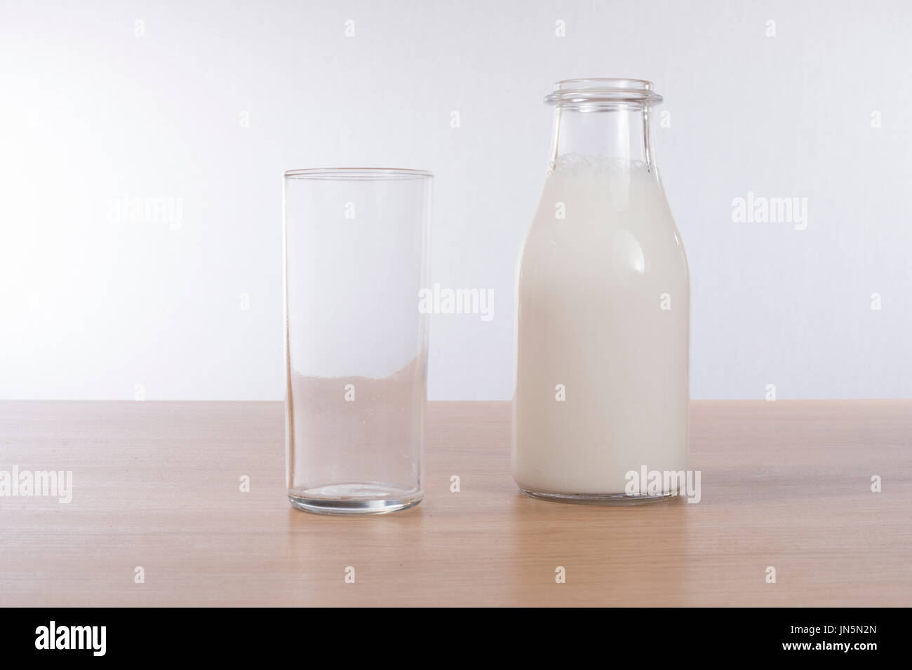 Ein Longdrinkglas leer trinken und eine Flasche frische Kuhmilch auf der Spitze eines einfachen Holzbank mit weißem Hintergrund und Kopie. Stockfoto