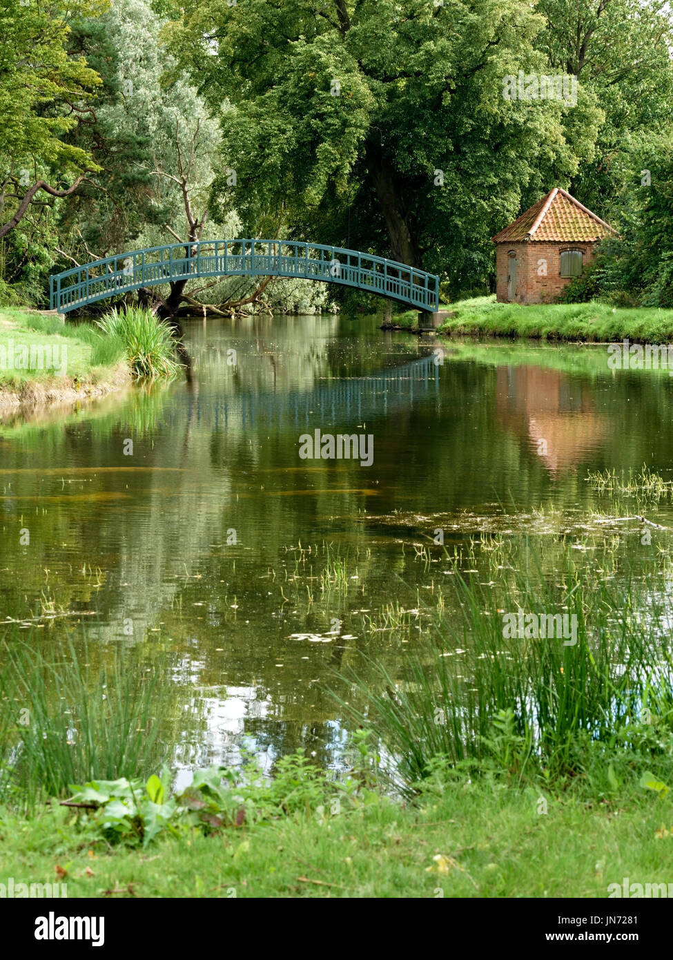 Ziemlich grün einzelne Bogen Fussgänger Holzsteg über den See auf dem Gelände des Doddington Hall Estate, Lincolnshire, England, UK Stockfoto