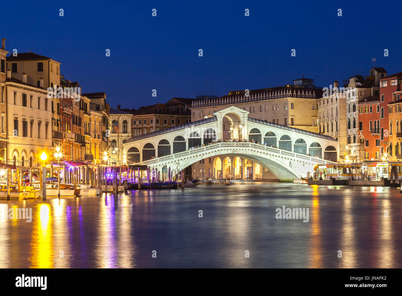 Venedig, Veneto, Italien Blick auf die Rialto-Brücke während der blauen Stunde mit Reflexionen auf dem Wasser und beleuchteten Pilazzos. Blick auf Langzeitbelichtung mit moti Stockfoto