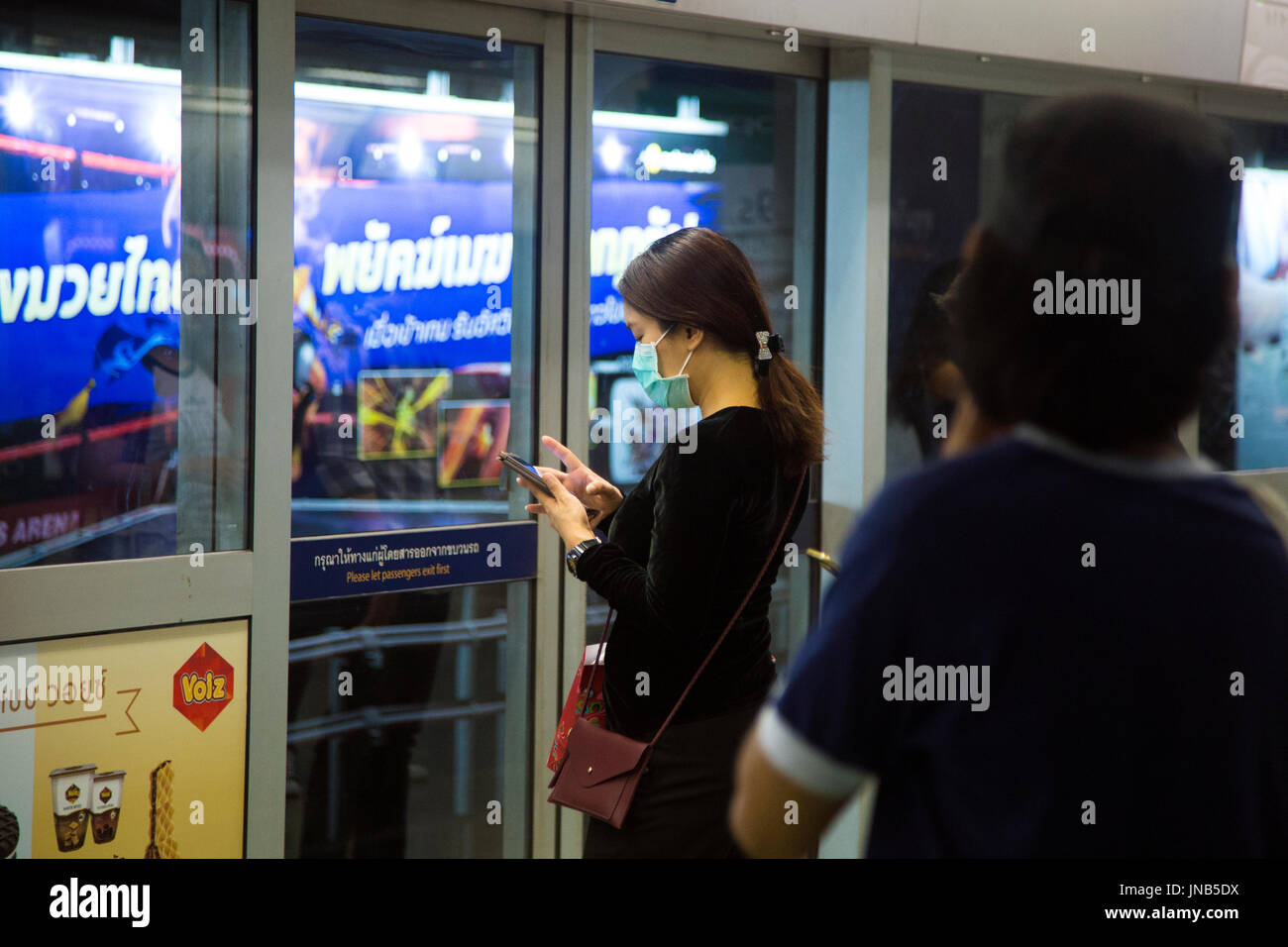Frau auf ihrem Handy trägt eine Maske zur Verbesserung des Umweltschutzes in der u-Bahn-Bangkok, Thailand Stockfoto