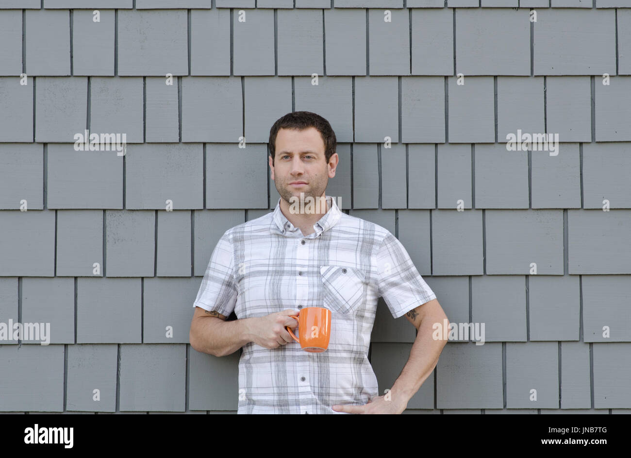 Mann mit Hand auf seiner Hüfte Holding eine Kaffeetasse gegen eine graue Wand. Stockfoto