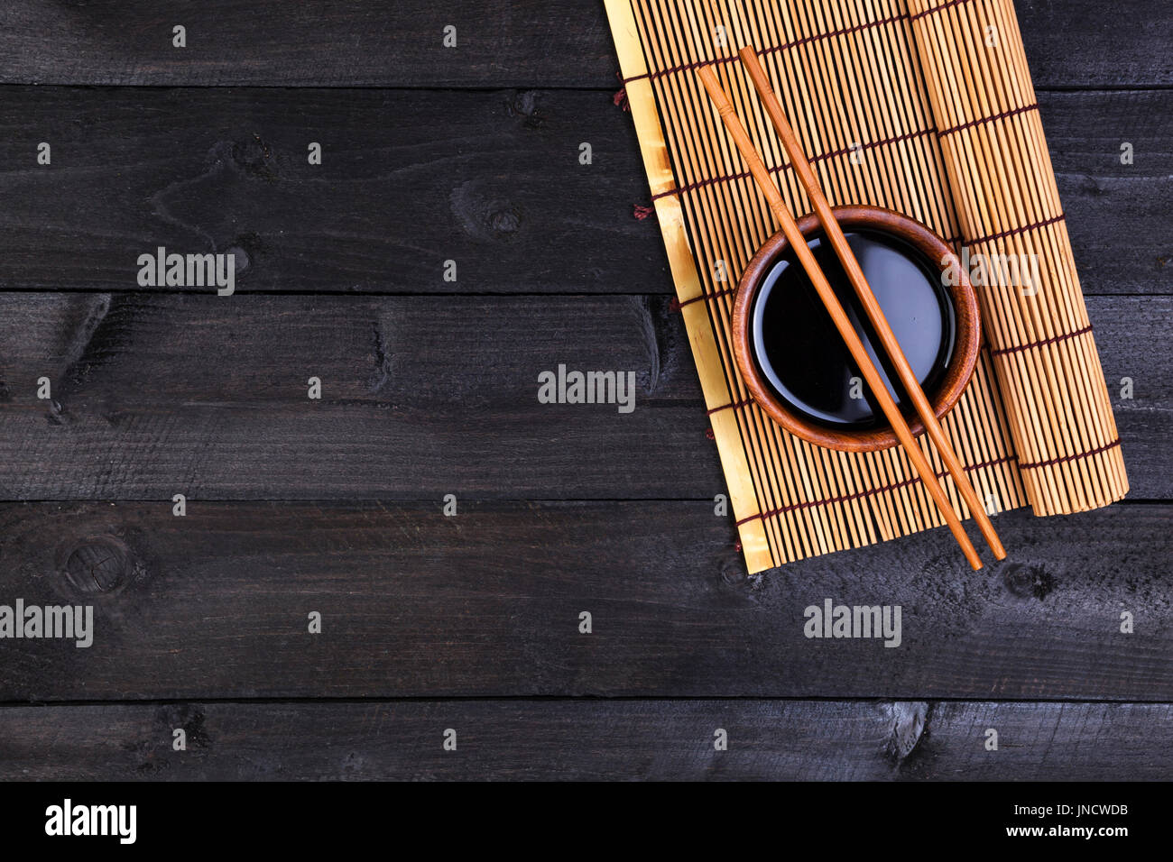 Hintergrund für Sushi. Bambusmatte und Sojasauce auf schwarzer Holztisch. Draufsicht mit Textfreiraum Stockfoto