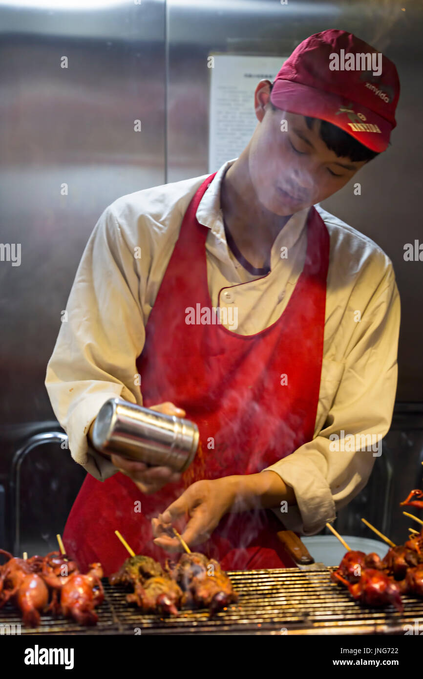 Chinesischen Verkäufer würzen Fleisch am Spieß auf traditionellen Lebensmittelmarkt. Wangfujing, Chaoyang District, Beijing, China, 5. April 2016 Stockfoto
