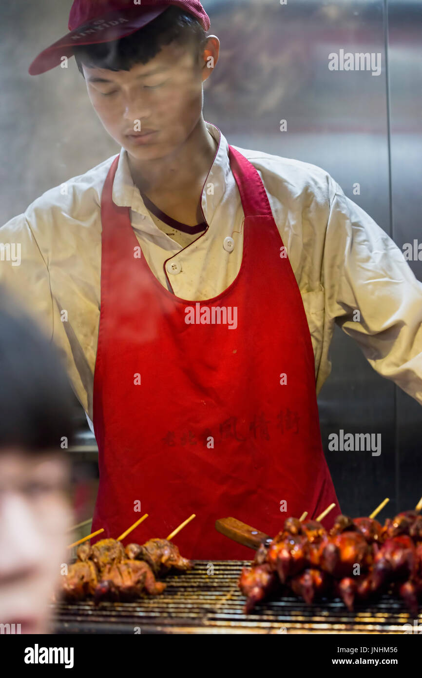 Chinesischen Verkäufer Zubereitung von Fleisch am Spieß auf traditionellen Lebensmittelmarkt. Wangfujing, Chaoyang District, Beijing, China, 5. April 2016 Stockfoto