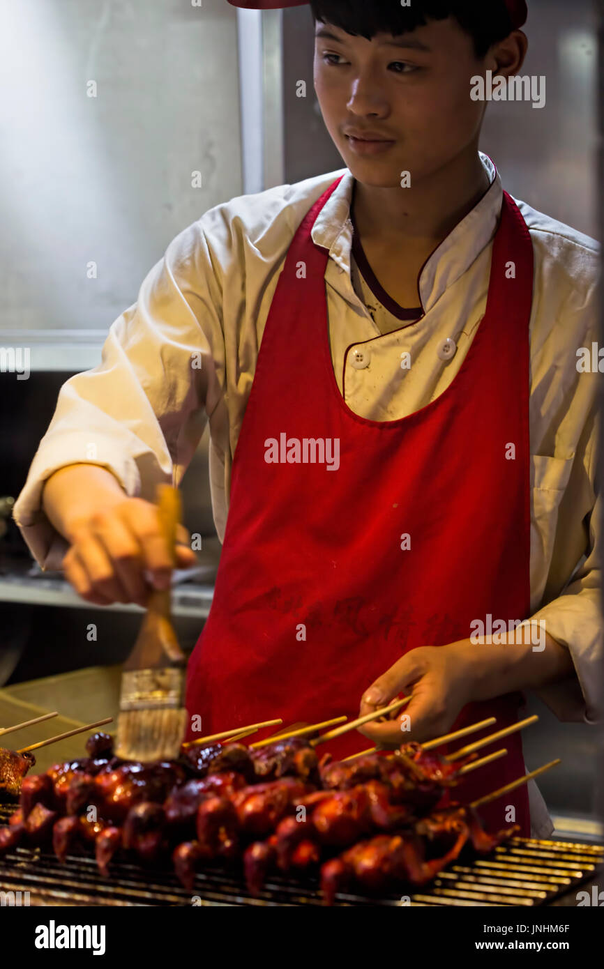 Chinesischen Verkäufer Zubereitung von Fleisch am Spieß auf traditionellen Lebensmittelmarkt. Wangfujing, Chaoyang District, Beijing, China, 5. April 2016 Stockfoto