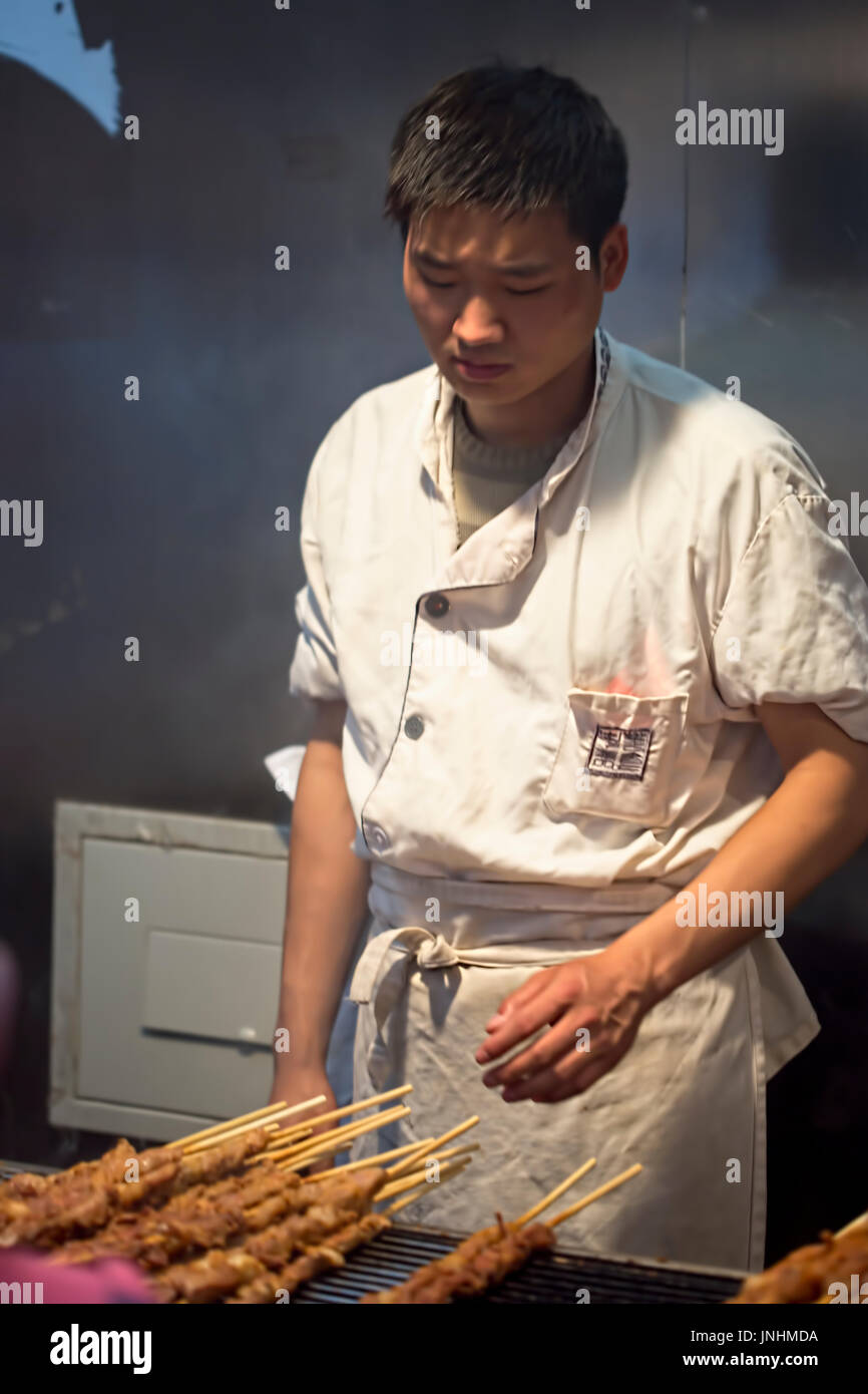 Chinesischen Verkäufer Zubereitung von Fleisch am Spieß auf traditionellen Lebensmittelmarkt. Wangfujing, Chaoyang District, Beijing, China, 5. April 2016 Stockfoto