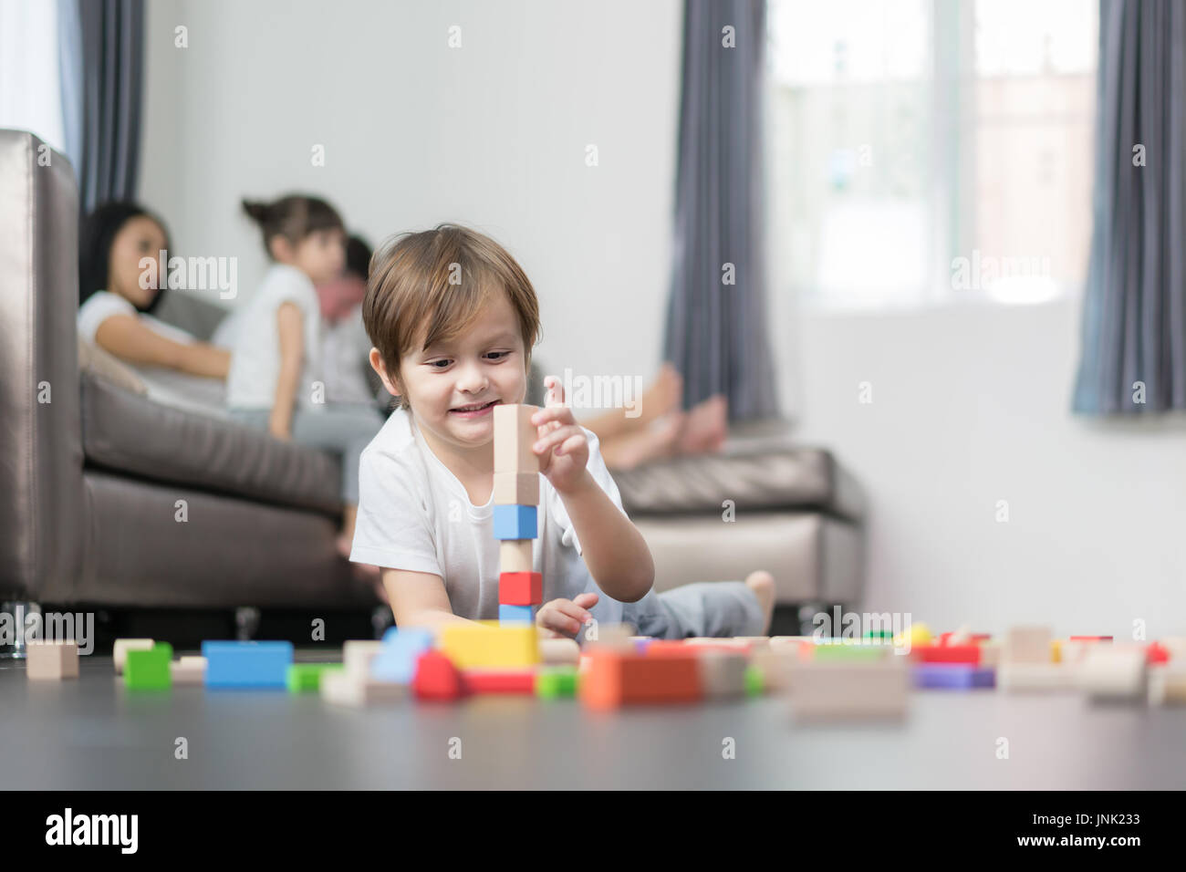 Asiatische junge Holz Spielzeug im Wohnzimmer mit Vater, Mutter und Tochter im Hintergrund zu spielen. Glückliche Familie. Stockfoto