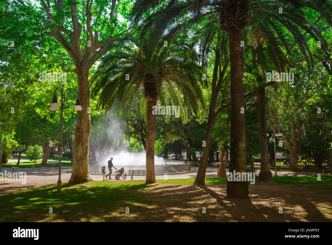 Vater und Kind, Blick auf einen Vater, der sein Kind in einem Kinderwagen durch einen Park in Italien schiebt, an einem Sommermorgen auf Sardinien, Italien, Stockfoto
