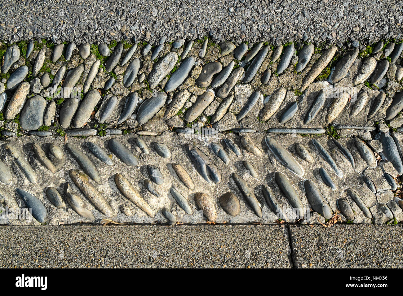 Dachrinne am Straßenrand gesäumt mit runden Steinen, Monein, Frankreich. Stockfoto