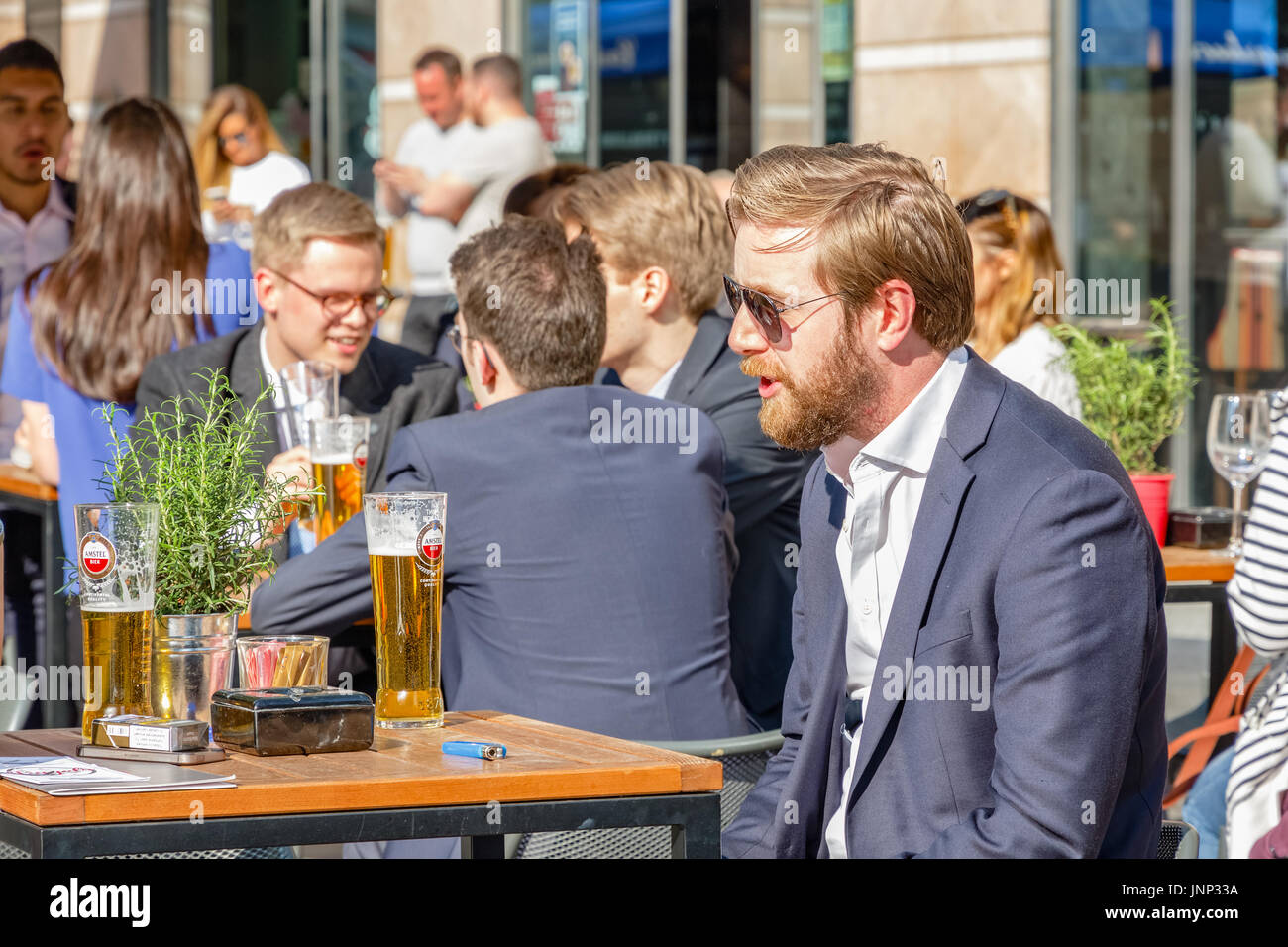 London, UK - 10. Mai 2017 - voller Leute trinken an einem sonnigen Tag ein junger Geschäftsmann in einer Outdoor-Bar in Canary Wharf Stockfoto