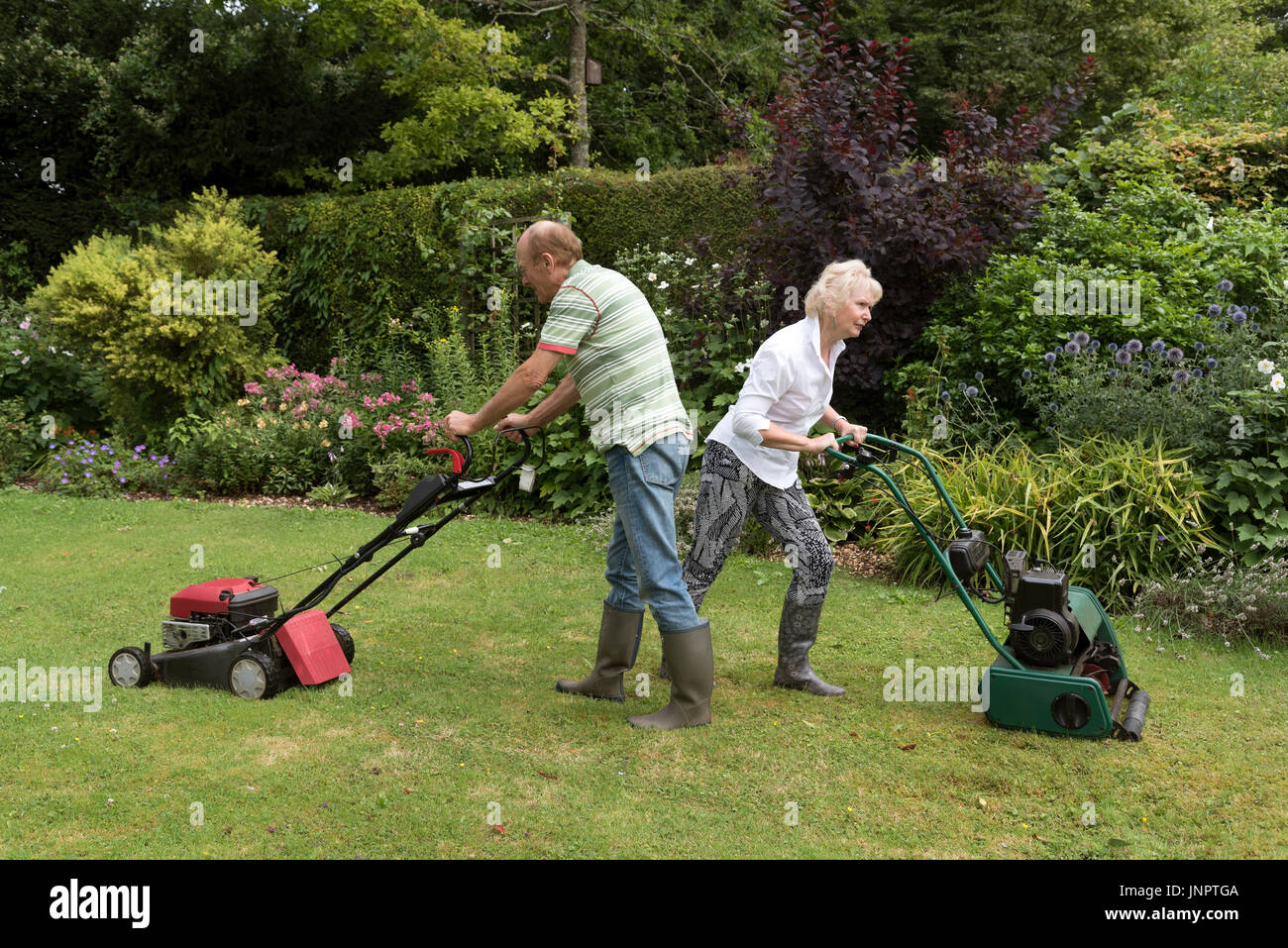 Mann und Frau mit Rasenmäher arbeiten in einen Garten. Stockfoto