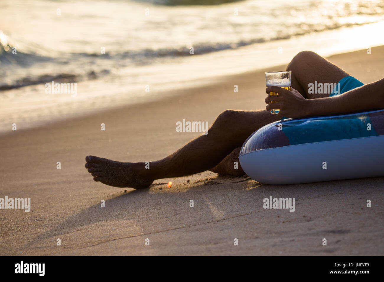 Nahaufnahme Mannhände und Beine mit einem Glas Bier auf Float Kreis, Gummischeibe am Strand sitzen. Sommer-Berufung Stockfoto