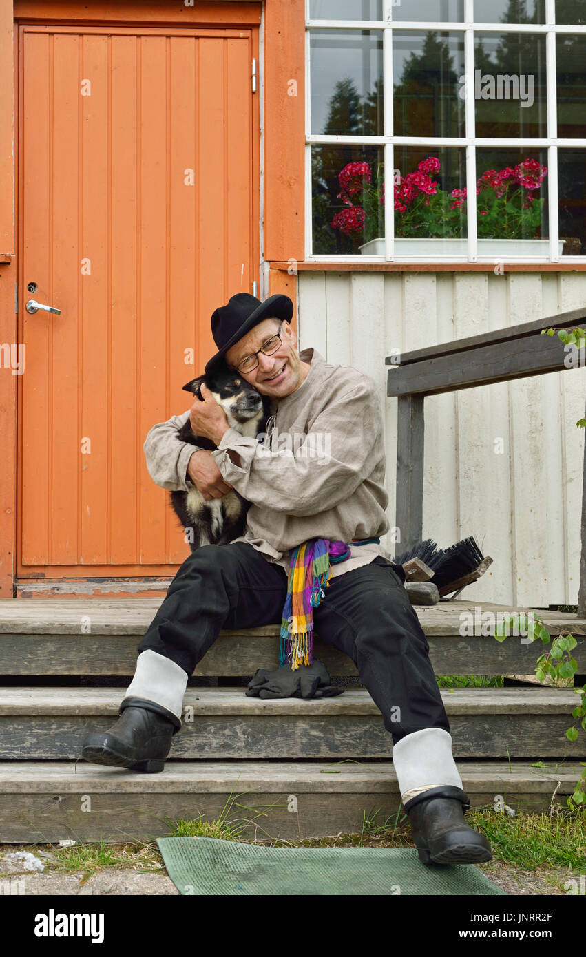 Landwirt in alten volkstümlichen Kleidung mit seinem Lieblingshund auf der Veranda seines Hauses. Finnisch-Lappland Stockfoto