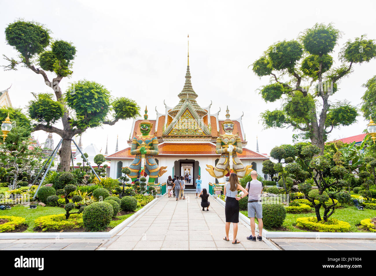 Der Eingang (Phra Ubosot) zu monastischen Viertel Komplexe mit riesigen Dämon zahlen und formgehölze Bäume am Wat Arun (Tempel der Morgenröte) in Bangkok, Thailand Stockfoto