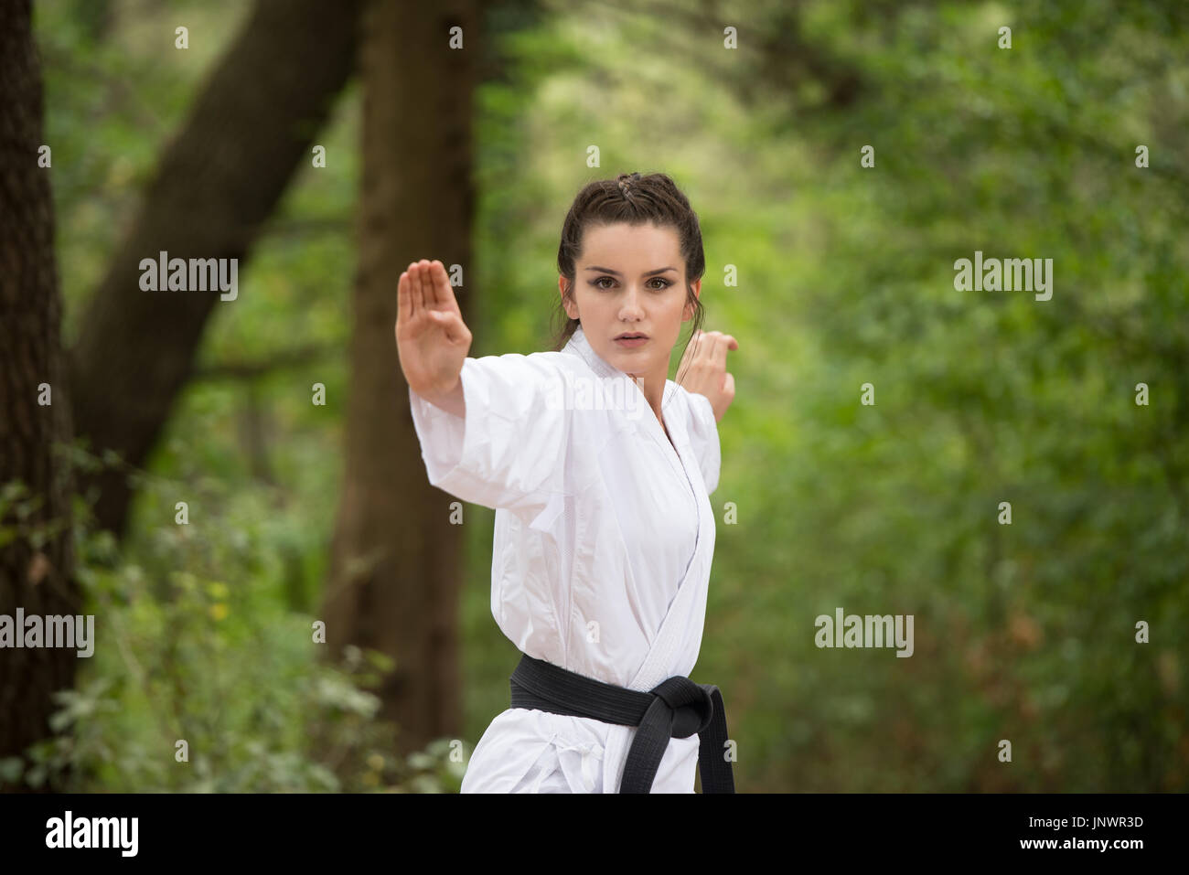 Junge Frau üben ihre Karate bewegt sich in bewaldeten Waldgürtel Bereich - weißen Kimono - schwarz Stockfoto