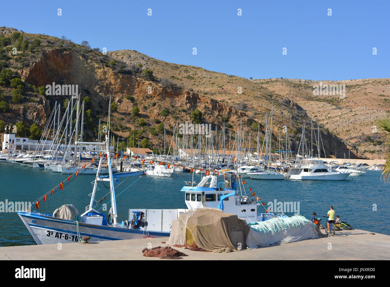 Fischkutter vertäut am Kai, mit Menschen, die Angeln vom Kai an einem heißen Sommertag in Javea an der Costa Blanca, Spanien. Stockfoto