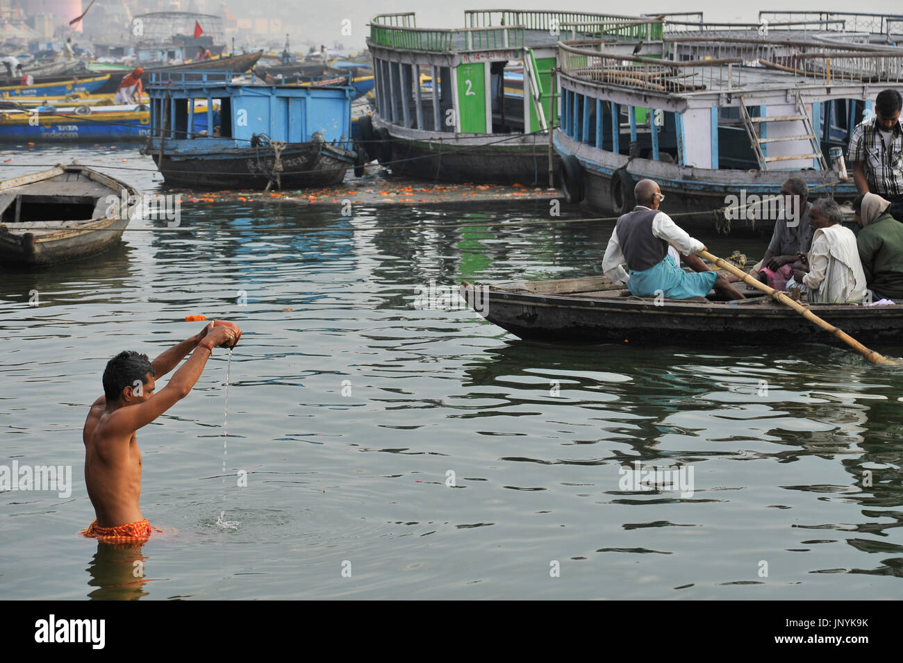 Ein Mann steht in den Heiligen Ganges und gießt das Wasser aus einem Tontopf Stockfoto