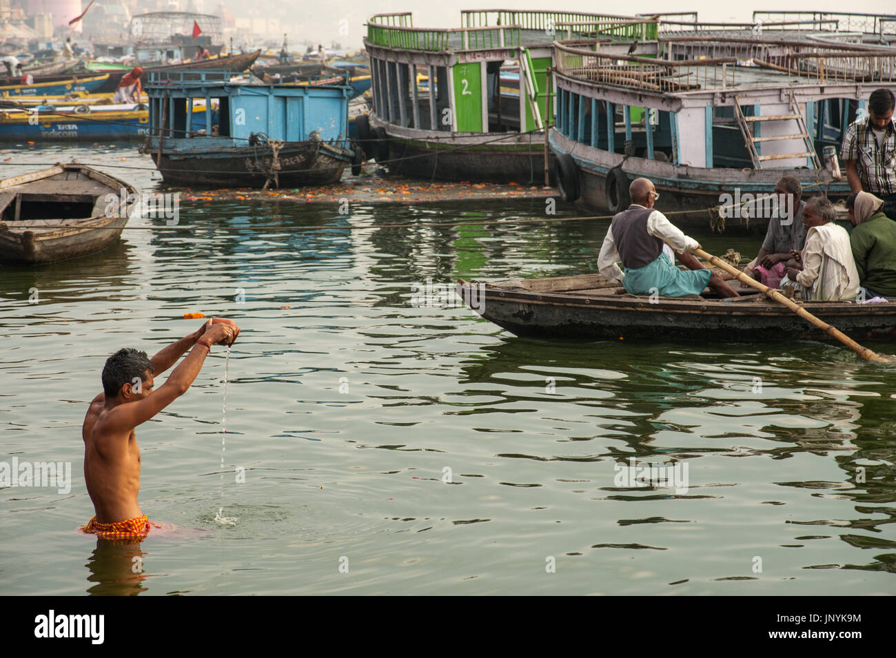 Ein Mann steht in den Heiligen Ganges und gießt das Wasser aus einem Tontopf Stockfoto