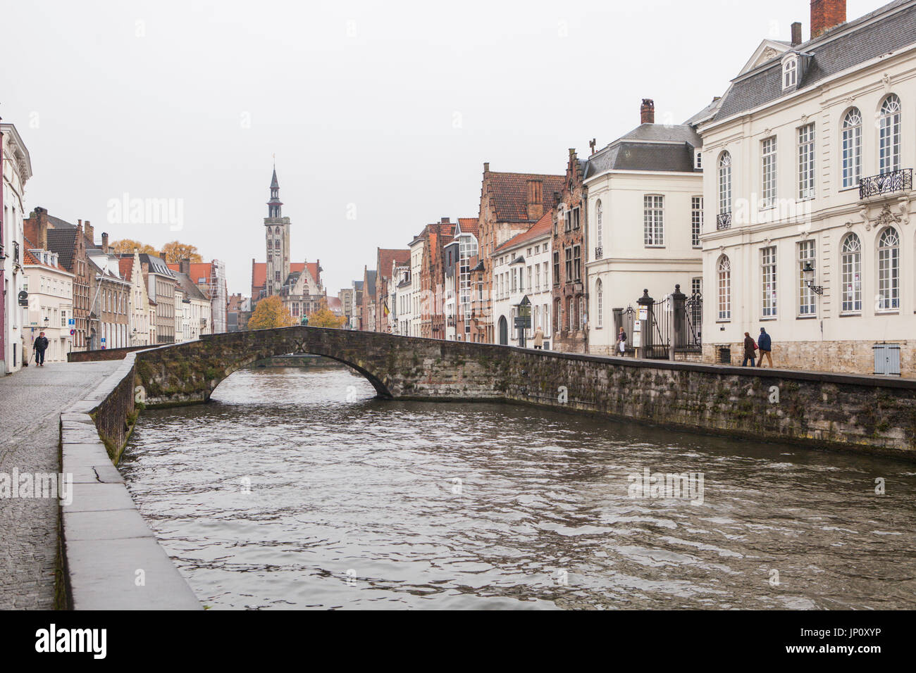 Brügge, Belgien – 31. Oktober 2010: ein paar Fußgänger im Regen auf Spinolarei, Koningstraat Brücke, die Statue von Van Eyck und die Poortersloge darüber hinaus. Brügge wird manchmal als das Venedig des Nordens bezeichnet. Stockfoto