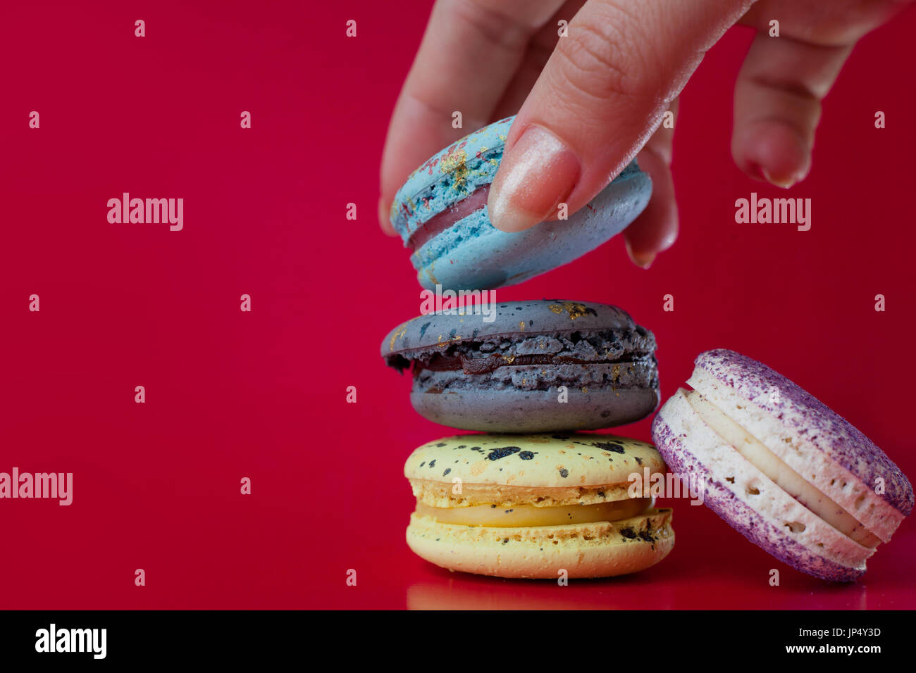 Viele Macarons. Roten Hintergrund. Weibliche Hand nimmt ein dessert Stockfoto