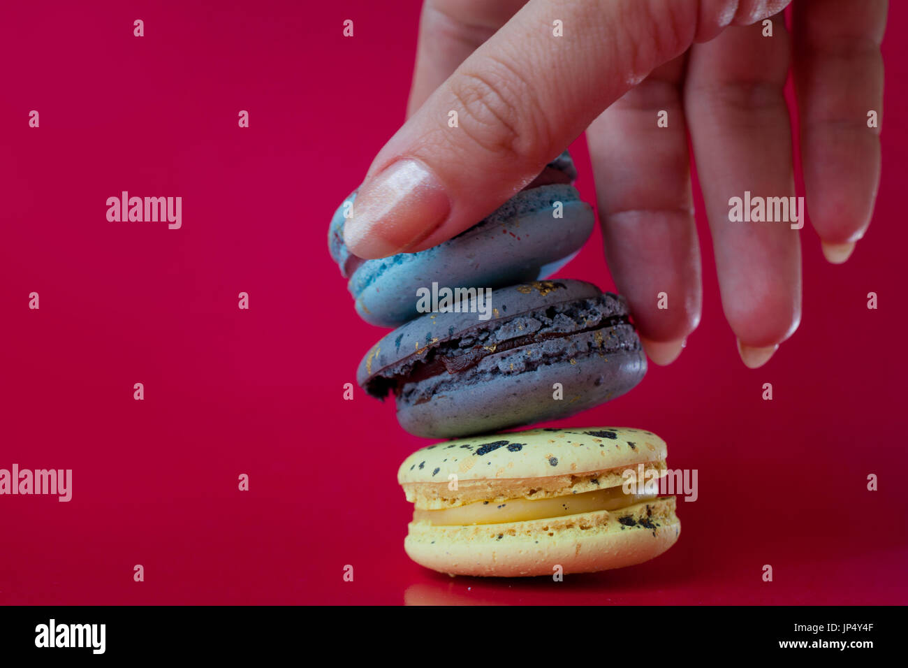 Viele Macarons. Roten Hintergrund. Weibliche Hand nimmt ein dessert Stockfoto