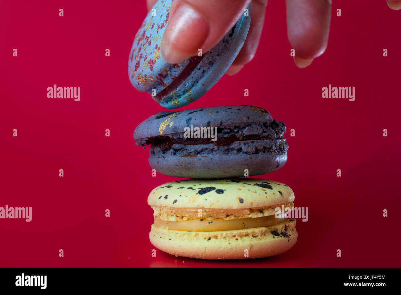 Viele Macarons. Roten Hintergrund. Weibliche Hand nimmt ein dessert Stockfoto