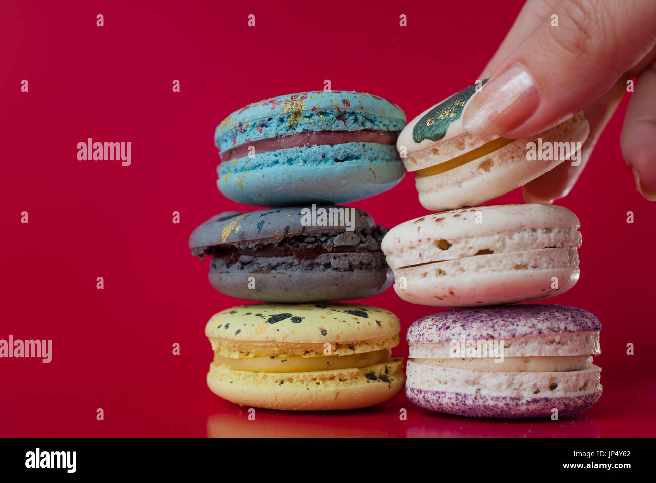 Viele Macarons. Roten Hintergrund. Weibliche Hand nimmt ein dessert Stockfoto