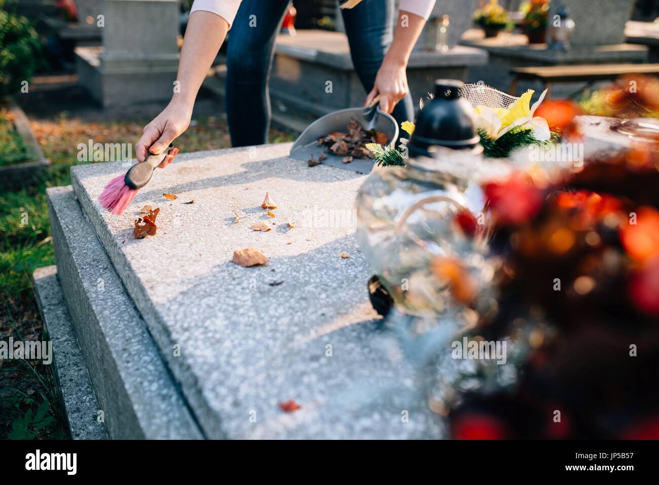 Eine Frau reinigt das Grab. Fegt Blätter aus dem Grabstein. Vorbereitungen für Allerheiligen am 1. November Stockfoto