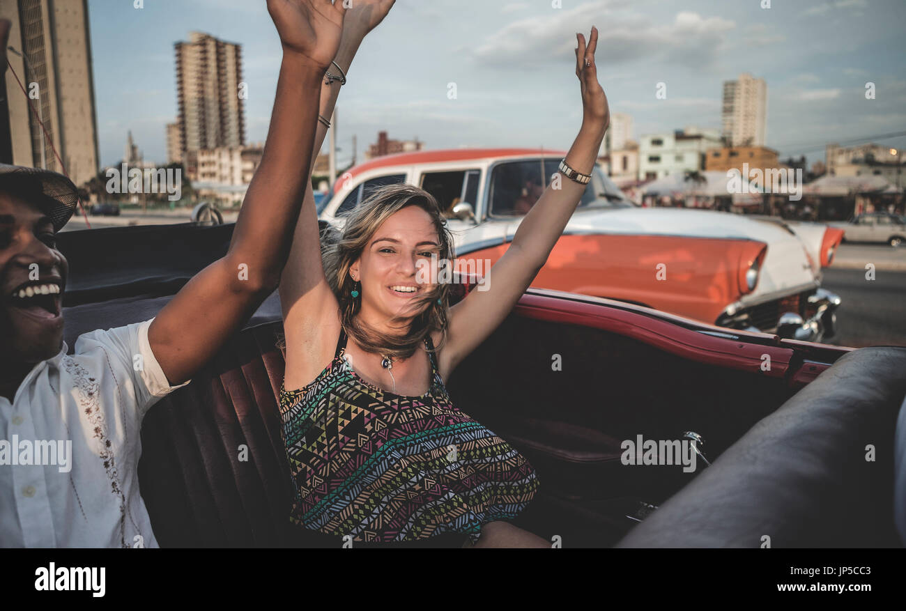 Zwei Personen Reiten durch eine Stadt in einem offenen Cabrio mit erhobenen Armen. Stockfoto