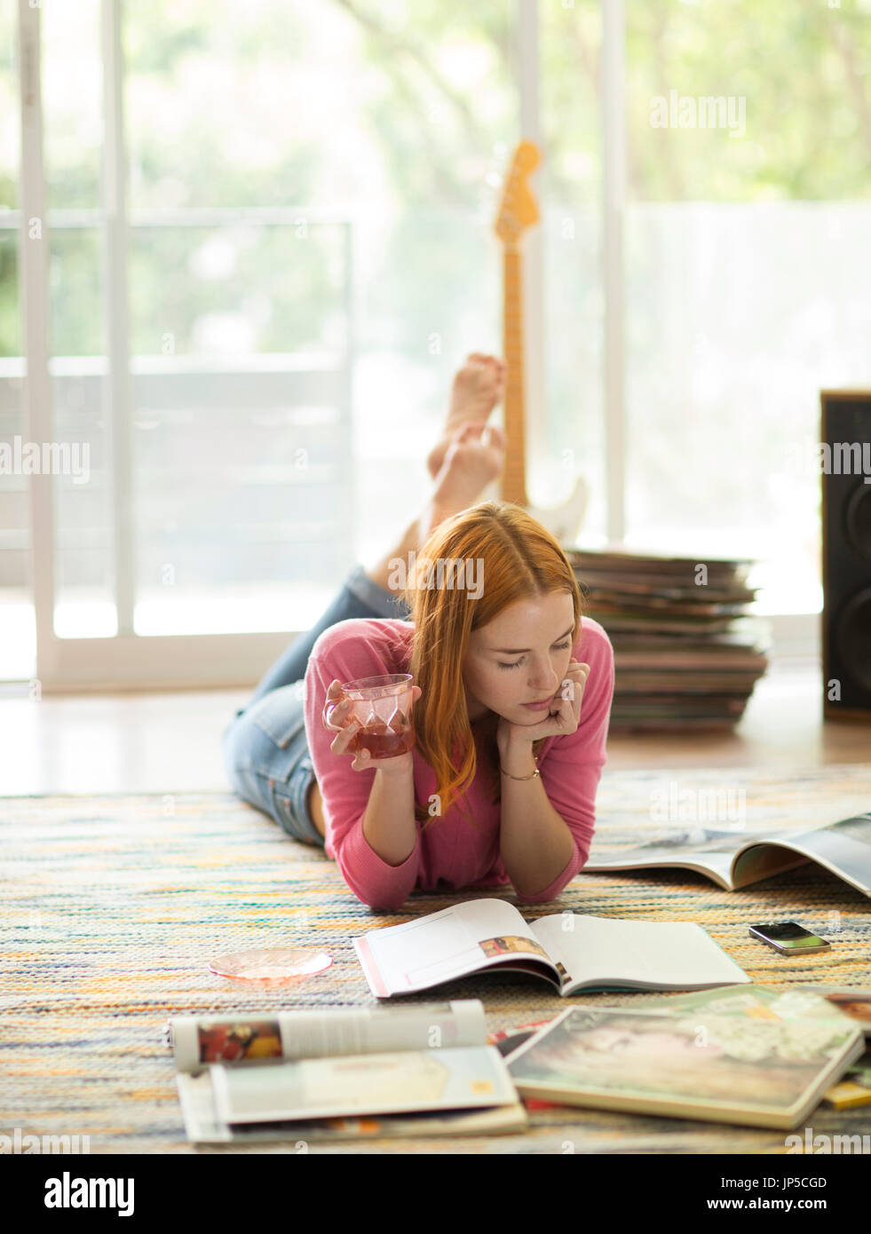 Eine Frau liegt auf dem Boden halten einen Drink und eine Zeitschrift liest. Stockfoto