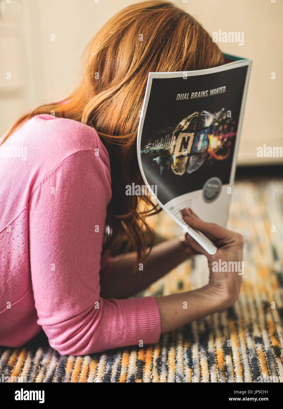 Eine Frau liegend auf einem Teppich und versteckt ihr Gesicht in einer Zeitschrift. Stockfoto