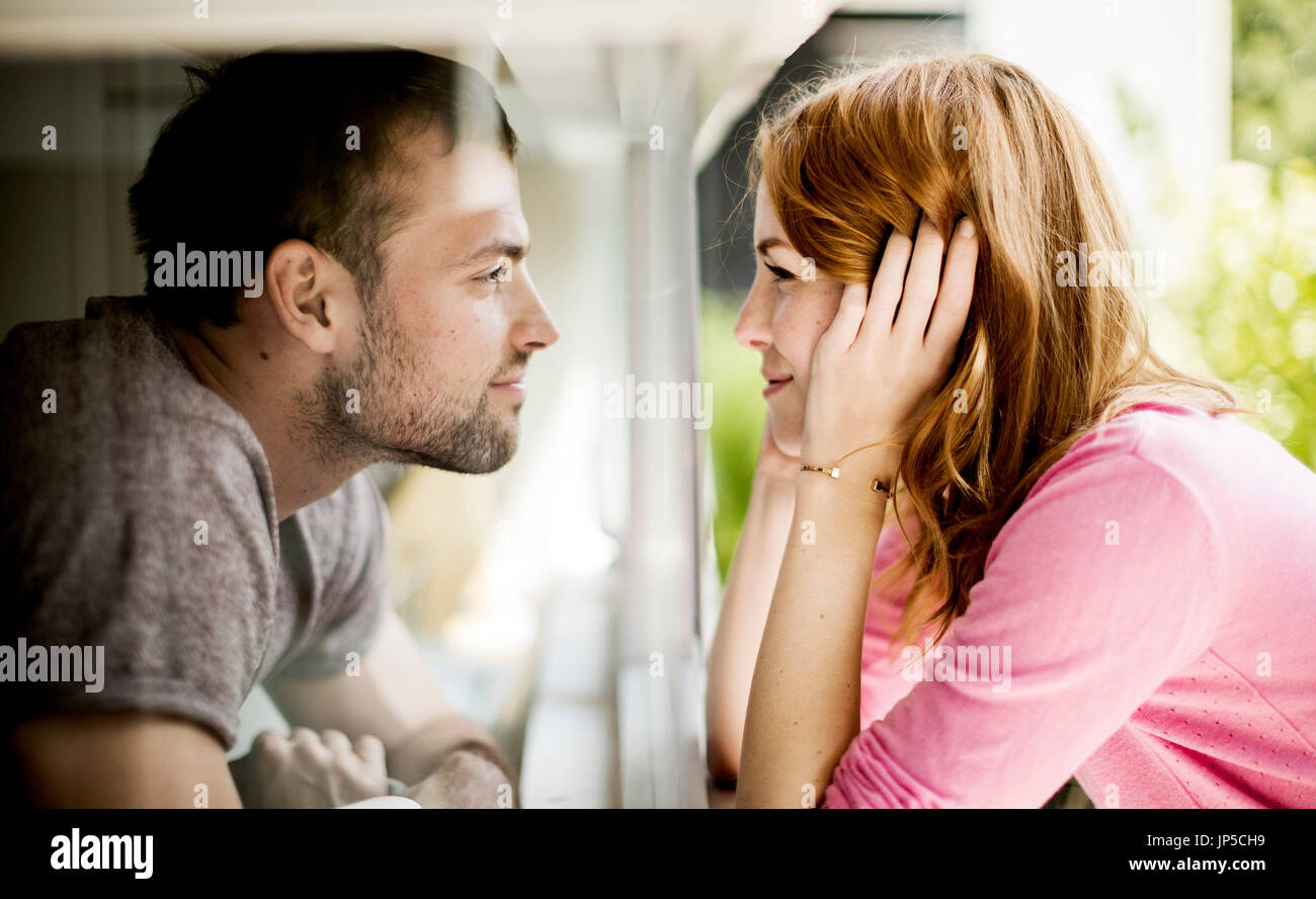 Ein paar lächelnd einander durch eine Glasscheibe eines Fensters. Stockfoto