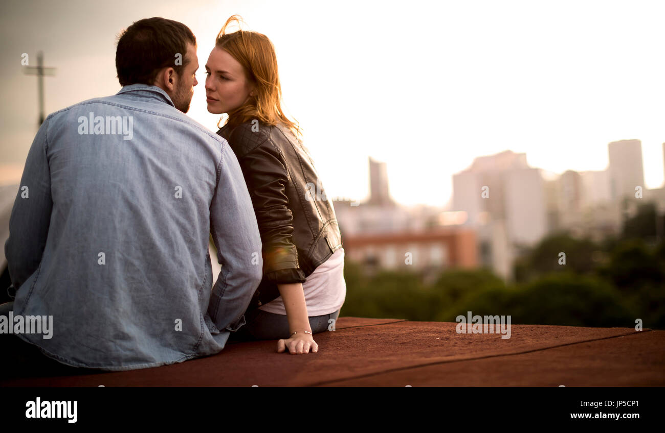 Ein paar sitzen und stützte sich für einen Kuss auf eine Stadt auf dem Dach. Stockfoto