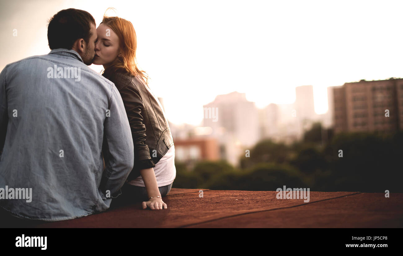 Ein paar sitzen und küssen auf den Dächern der Stadt. Stockfoto