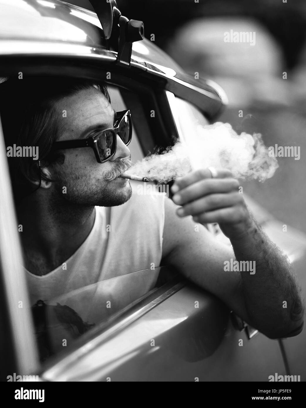 Mann mit Schnurrbart gelehnt aus Autofenster, Sonnenbrille, Rauchen eine Zigarette, Zigarette zu rauchen. Stockfoto