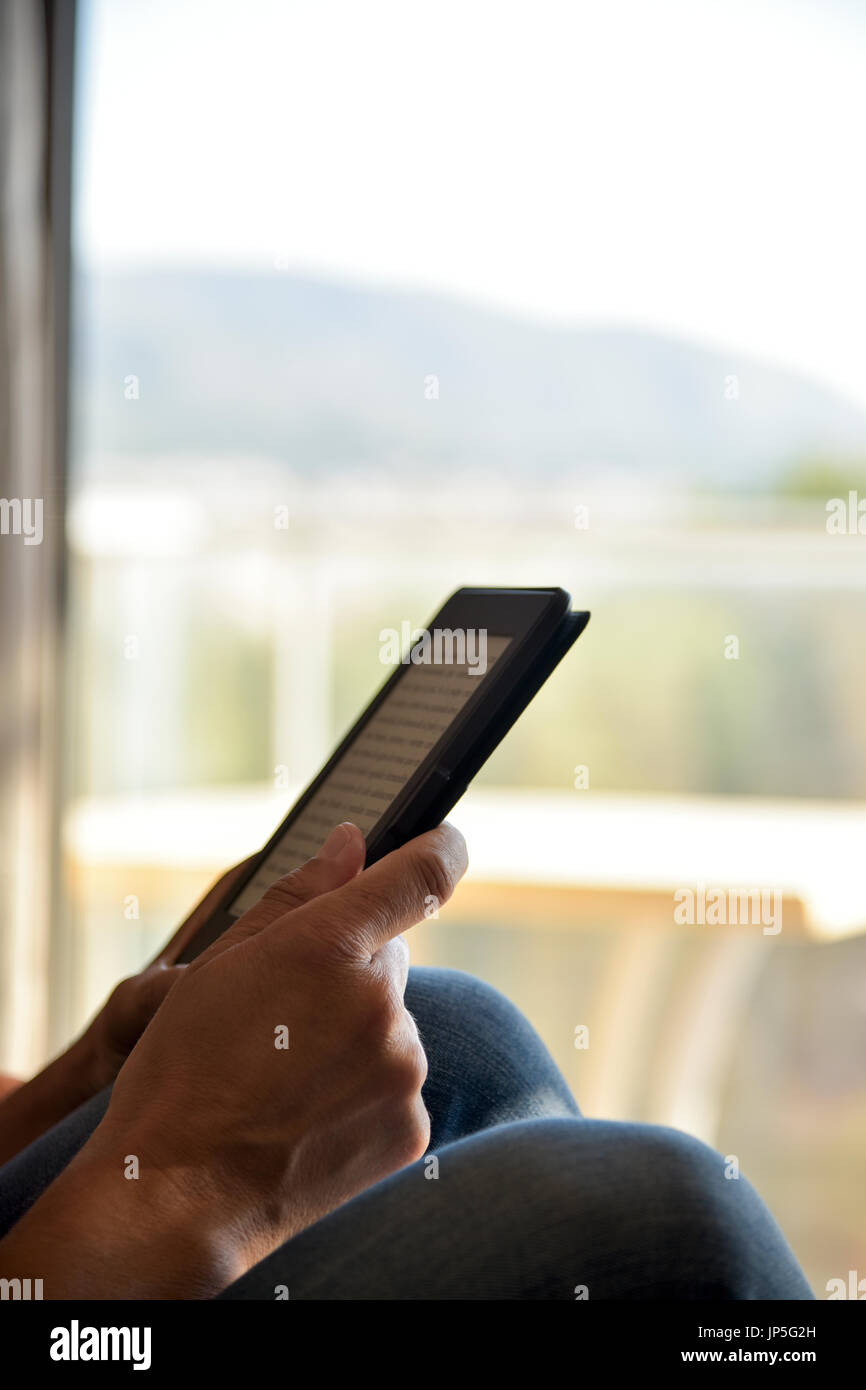 Closeup von einem kaukasischen Jüngling trägt Jeans, lesen in einem Tablet oder e-Reader neben einem Balkon Stockfoto