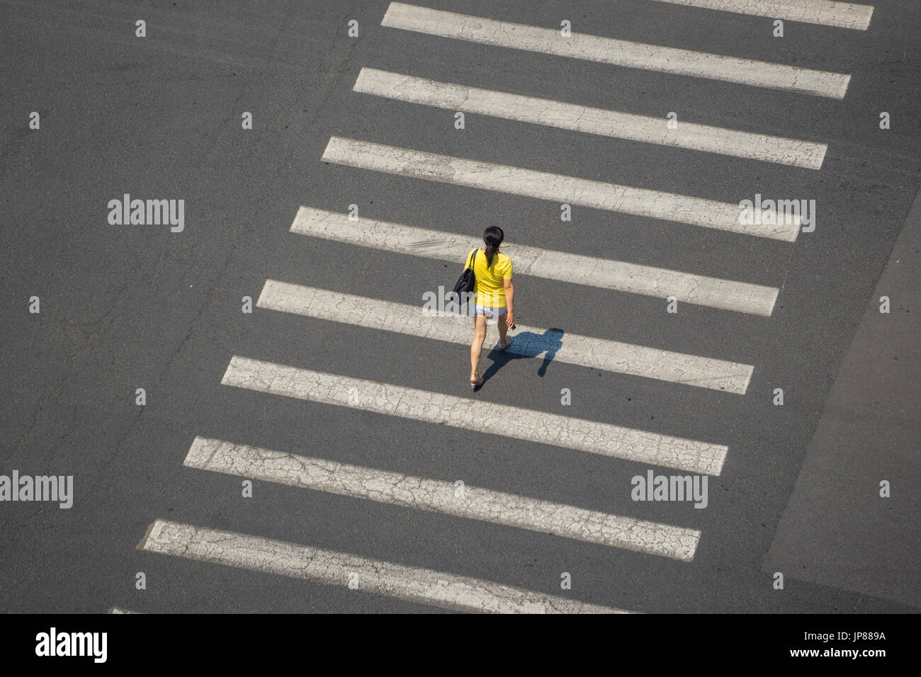 Luftaufnahme der Frau in gelb Top walking mit Schatten über Linien der Zebrastreifen eine breite Straße Stockfoto