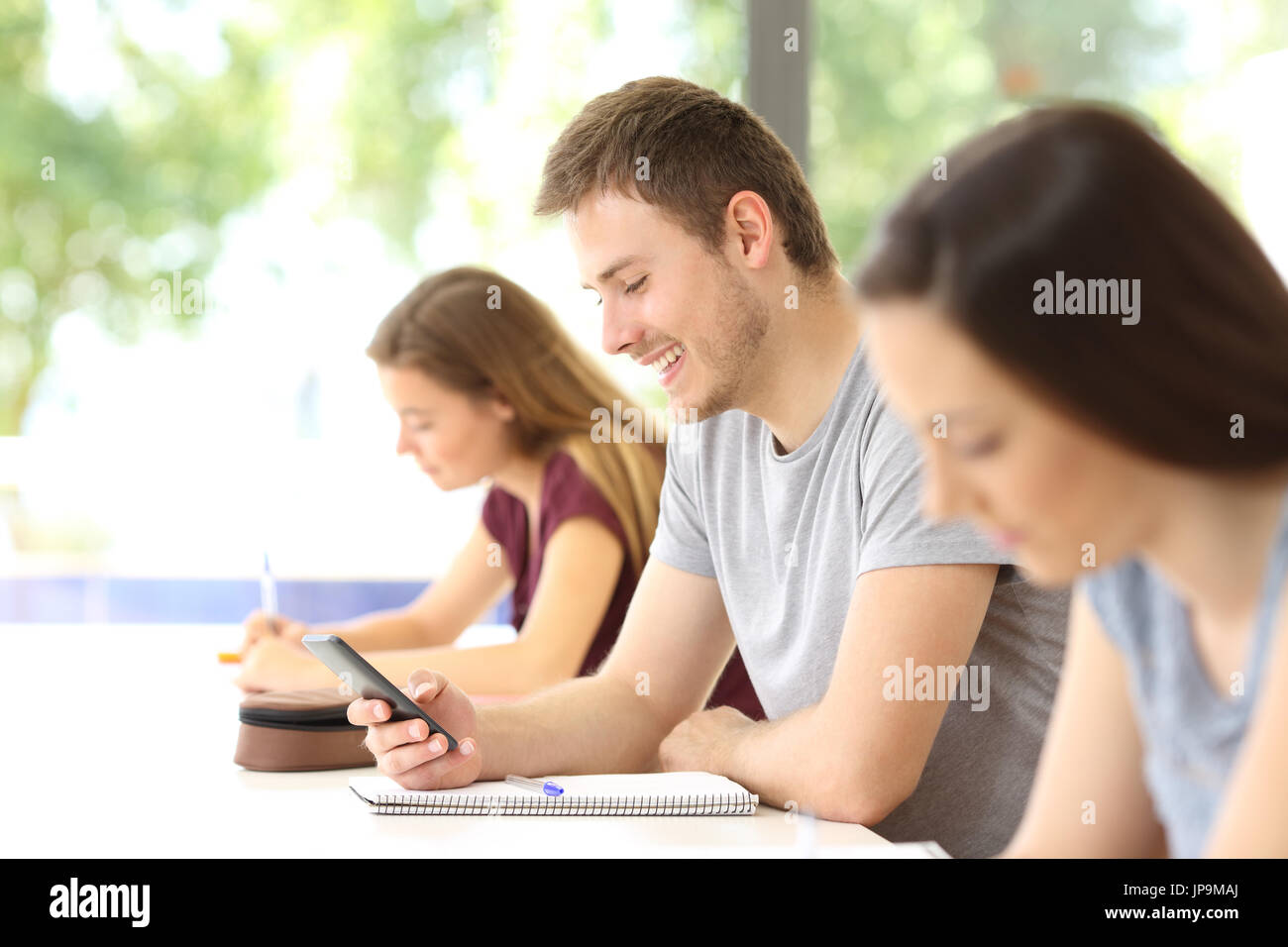 Seitenansicht eines Studenten mit einem Mobiltelefon, während eine Klasse abgelenkt im Klassenzimmer Stockfoto