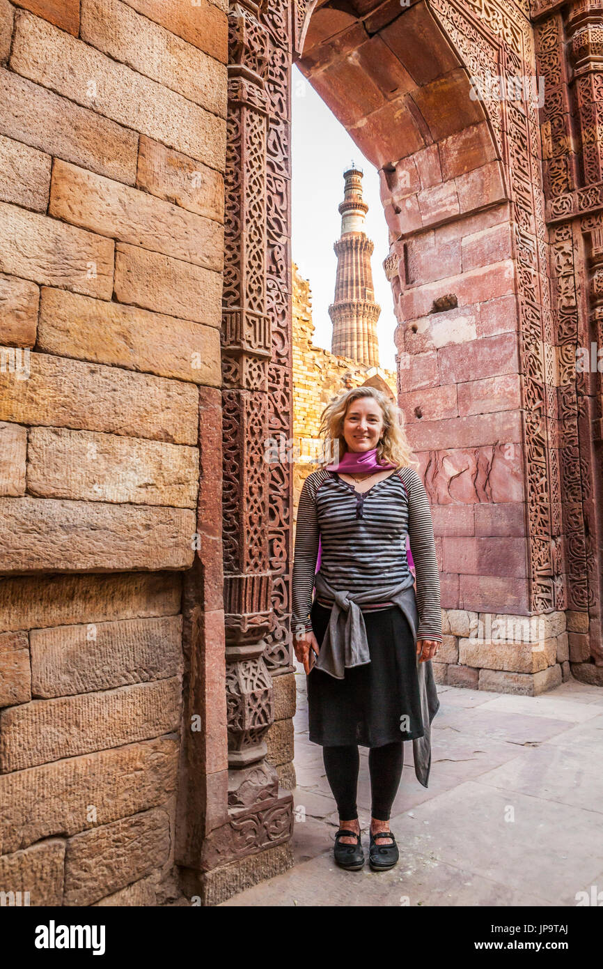 Eine weibliche westliche Touristen stehen für ein Bild in einem Torbogen mit der Qutb Minar im Hintergrund, Delhi, Indien. Stockfoto