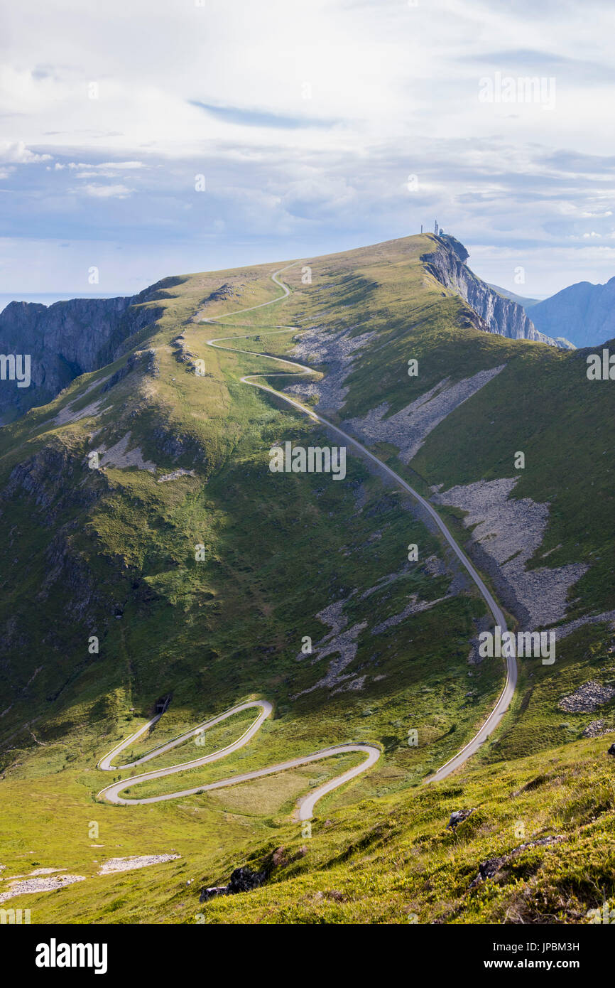 Steile Straße von Kurven auf der grünen Wiese umrahmt von felsigen Gipfeln Sorland Vaeroy Insel Grafschaft von Nordland Lofoten Norwegen Europa Stockfoto