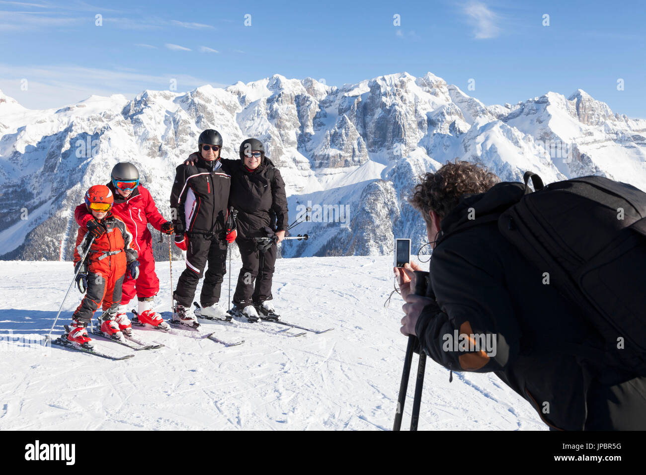 ein Skifahrer macht ein Foto zu einer Familie in ihrem Winterurlaub im Trentino mit der Brenta-Gruppe im Hintergrund, Provinz Trento, Trentino Alto Adige, Italien, Europa Stockfoto